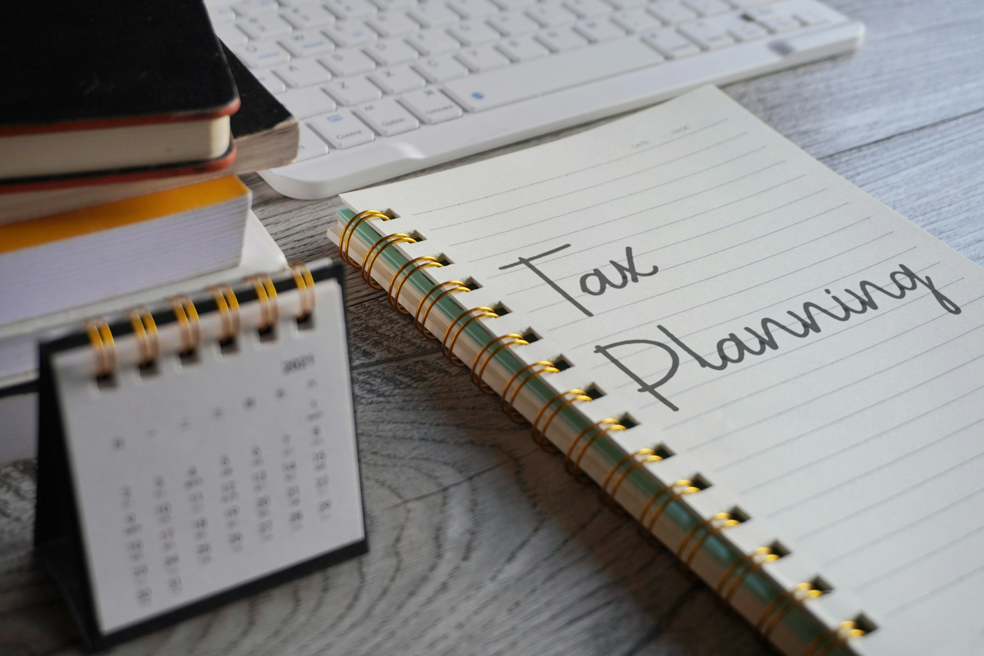 Closeup image of notebook with text TAX PLANNING and calendar on office desk.